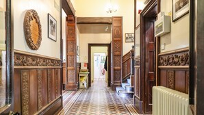 Um corredor com painéis de madeira ornamentados, piso de azulejos estampados e um radiador à direita.