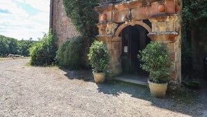 Um edifício histórico com fachada de pedra, arco de madeira e plantas em vasos na entrada.