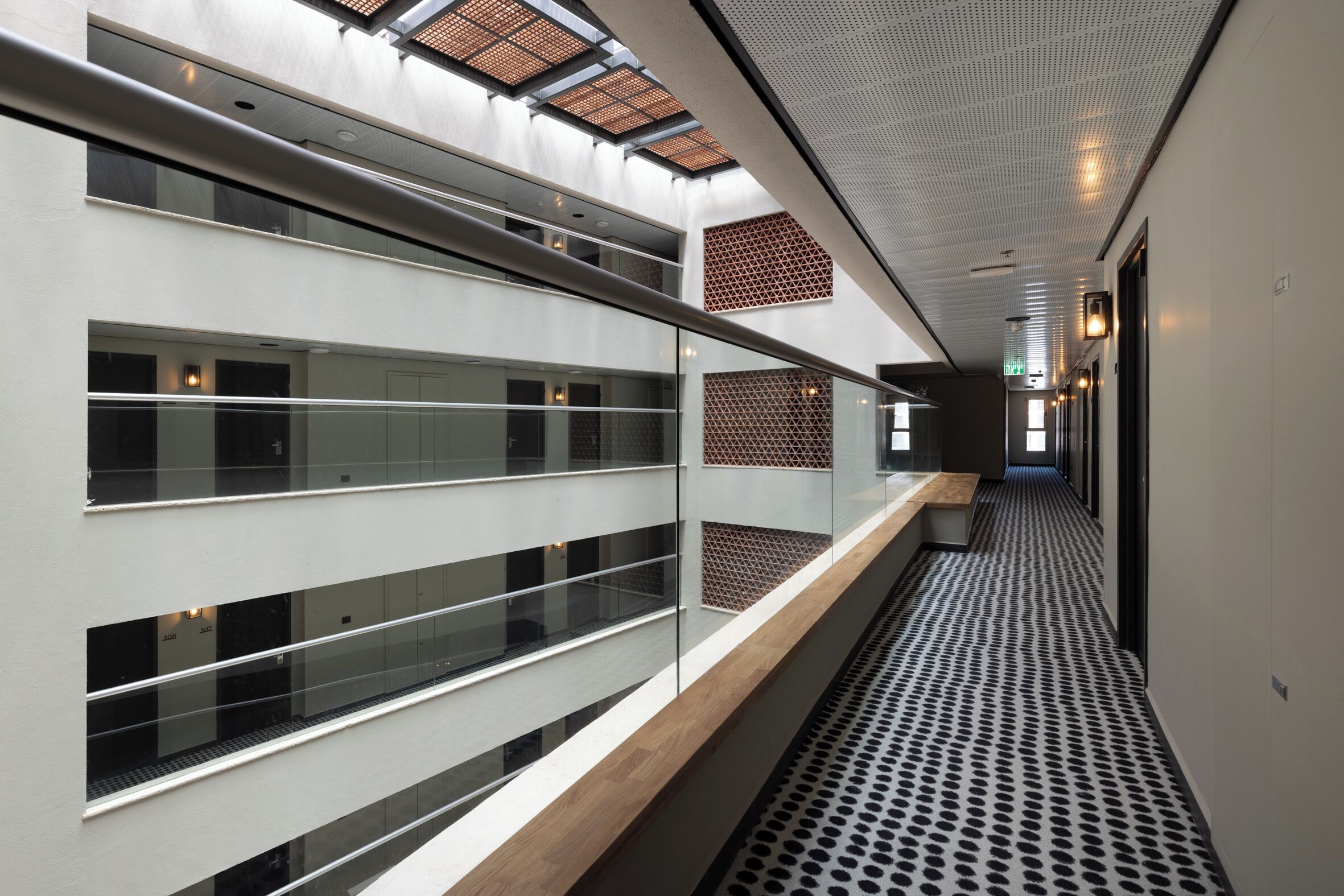 A modern interior with a long corridor, glass railings, and a patterned floor.