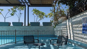 Área de piscina externa com bancos e plantas em vasos.