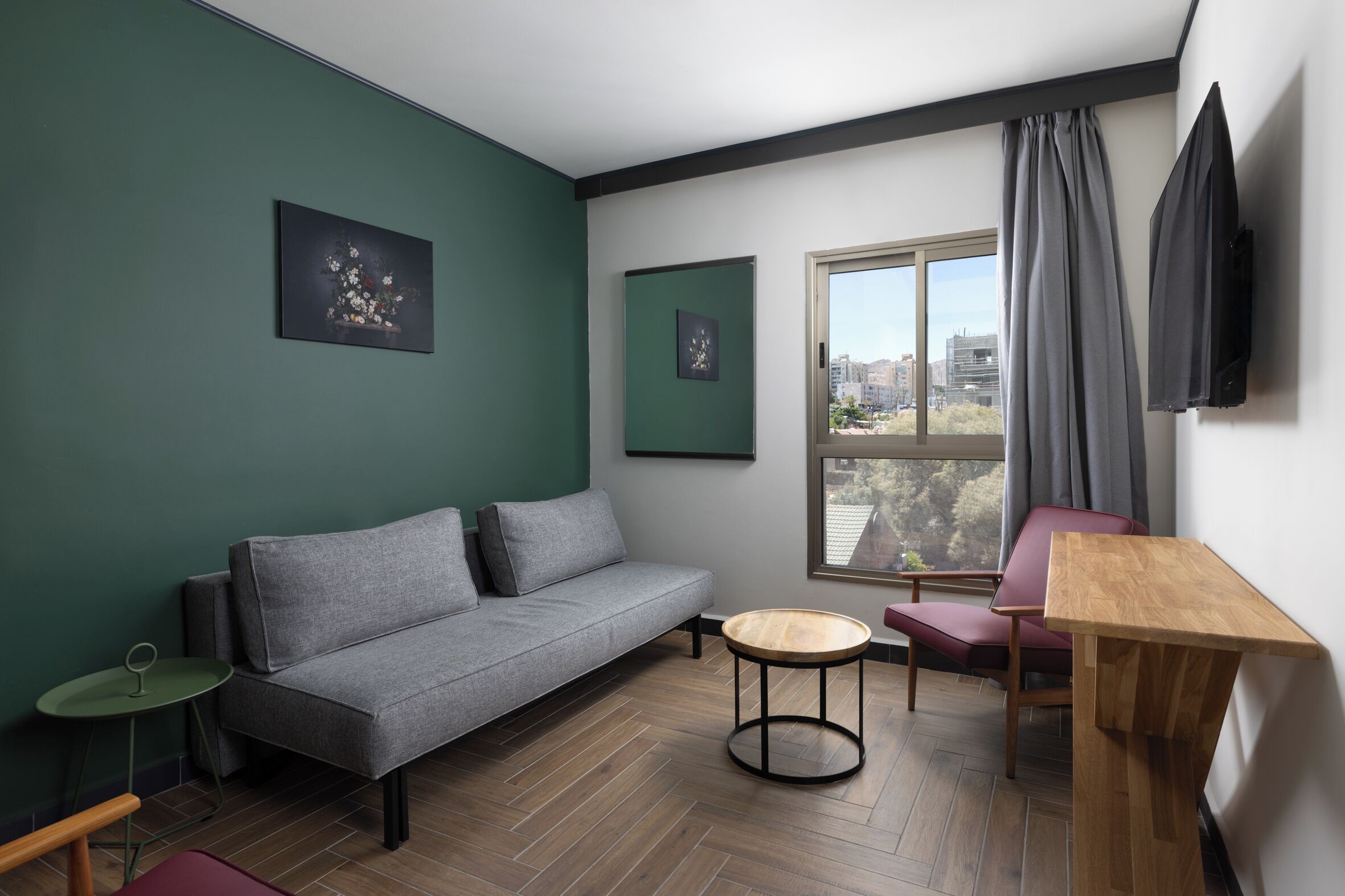 A modern living room with a grey sofa, a small round wooden table, a red chair, and a TV mounted on the wall.