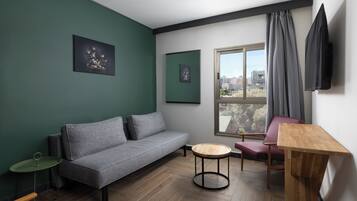 A modern living room with a grey sofa, a small round wooden table, a red chair, and a TV mounted on the wall.