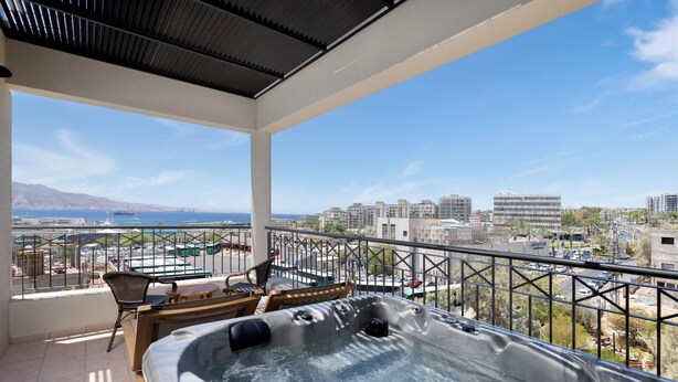 Uma varanda com hidromassagem, cadeiras e vista para a paisagem urbana e o mar.