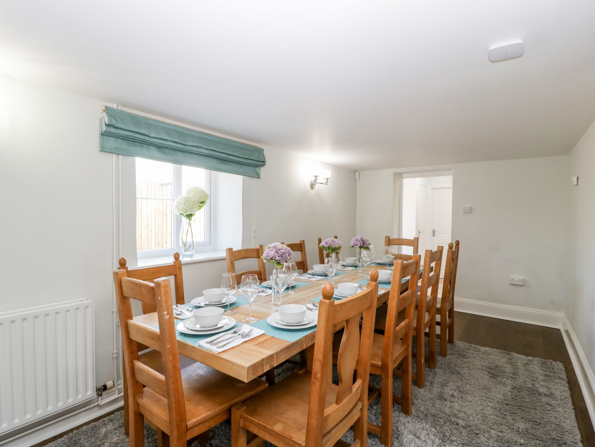 A dining room with a wooden table set for six, flanked by chairs.