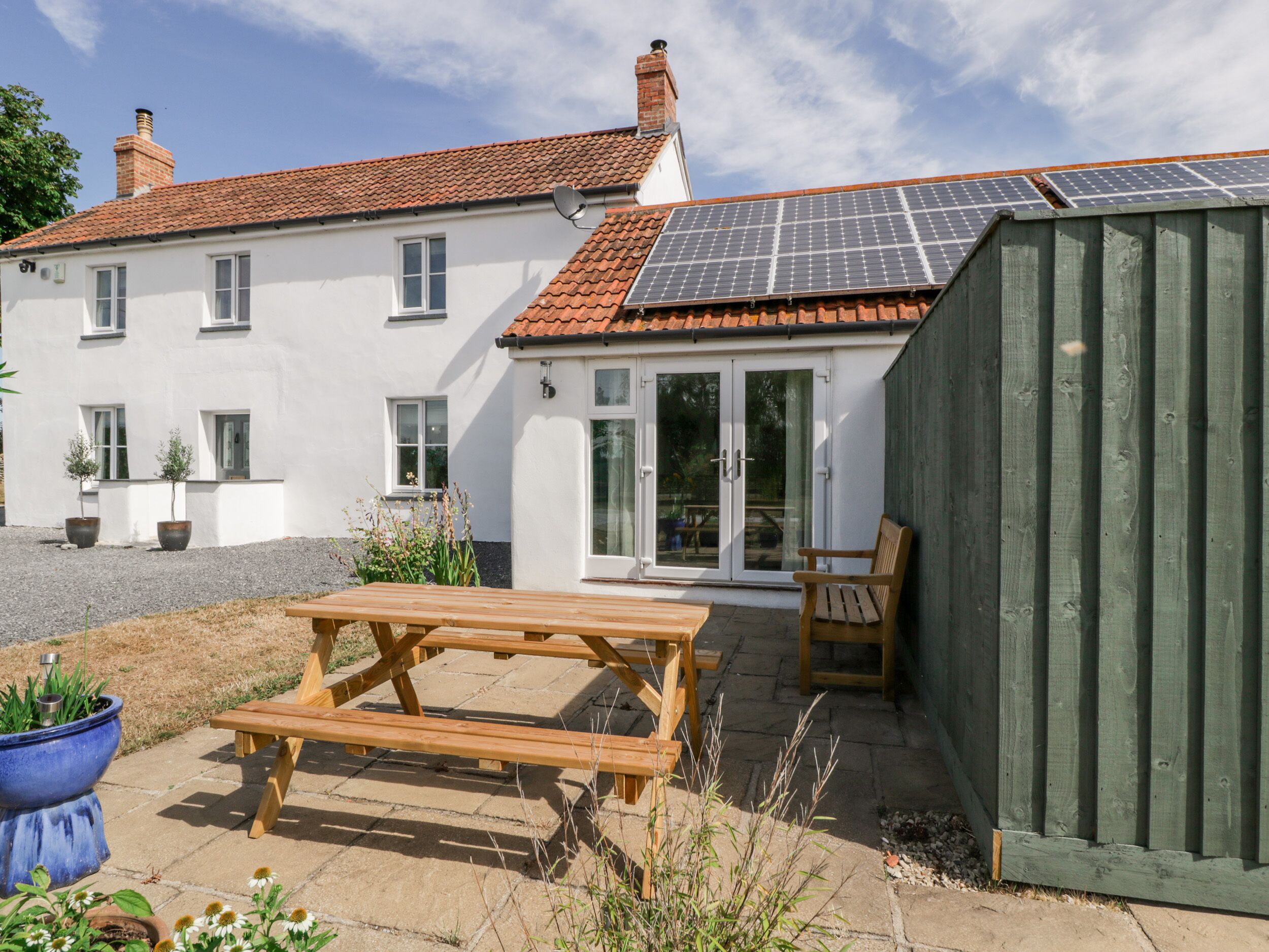 A house with a solar panel roof, a patio with a wooden table and chairs, and a green shed.