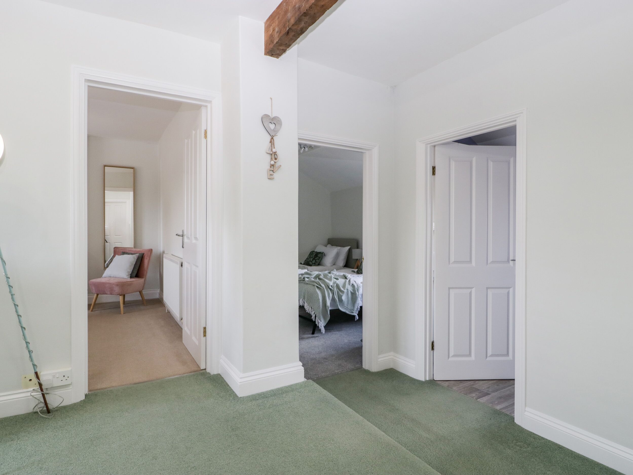 A hallway with a green carpet, a pink chair, a white door, and a bed with a green blanket.
