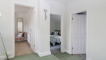 A hallway with a green carpet, a pink chair, a white door, and a bed with a green blanket.
