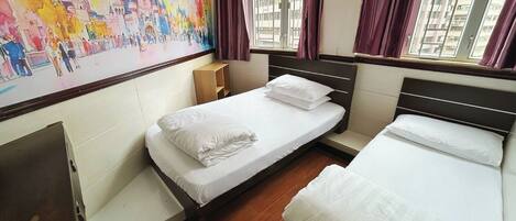 A hotel room with a large mural of a castle, a single bed with white bedding, a wooden nightstand, and a window with purple curtains.