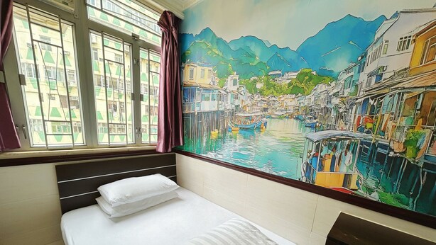 A hotel room with a bed, a window with curtains, and a mural of a riverside town. - National Inn HK (Kowloon)