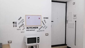 A compact kitchen with a microwave, a small shelf, and a sink. There is a wall-mounted sign with words related to food and drink. - Apartment 500 meters from the Central Station. (Napoli)