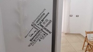 A room with a white wall featuring a vertical text message in multiple languages, a wooden chair, and a potted plant. - Apartment 500 meters from the Central Station. (Napoli)