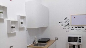 A compact kitchen with white cabinetry, a microwave, and a small countertop. There are potted plants on shelves and a dining table set with plates and cutlery. - Apartment 500 meters from the Central Station. (Napoli)