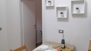 A dining area with a table set for two, a wooden chair, and a wall-mounted shelf with a potted plant. - Apartment 500 meters from the Central Station. (Napoli)