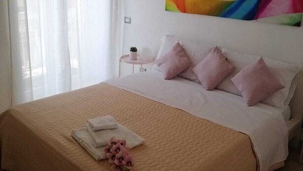 A neatly made bed with a beige quilt, pink pillows, and a small bouquet of pink flowers on the bed. - Apartment 500 meters from the Central Station. (Napoli)