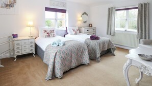 A bedroom with two beds, a dresser, a nightstand, and a table with a bowl. - Willow Cottage (Norwich)
