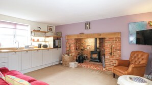 A cozy living room with a fireplace, a red sofa, a wooden chair, and a television. - Willow Cottage (Norwich)