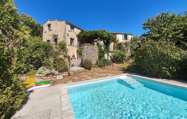 Relax by the serene pool surrounded by lush greenery and traditional buildings.