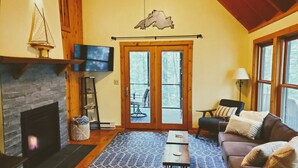 Una sala de estar acogedora con chimenea, un televisor montado sobre ella y un ventanal con vistas al exterior.