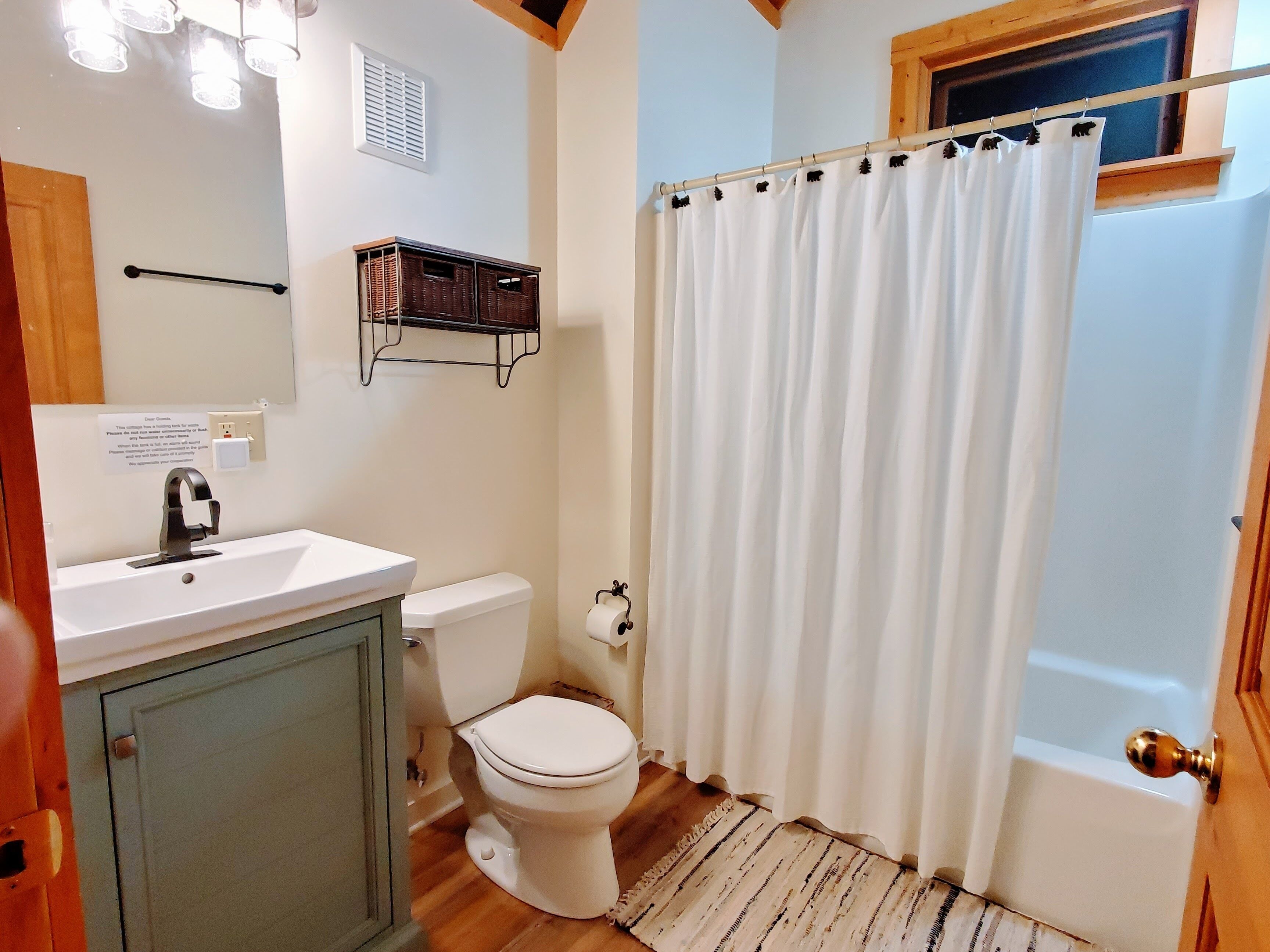 A bathroom with a white sink, toilet, and shower curtain. There is a wooden floor and a small rug near the shower.