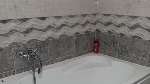 Ein modernes Badezimmer mit freistehender Badewanne, einer Duschbrause und einer roten Shampoo-Flasche an der Wand.