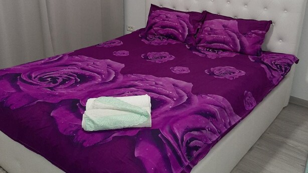 Ein Bett mit weißem Kopfteil und einer violetten, blumengemusterten Tagesdecke.