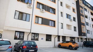 Ein mehrgeschossiges Wohngebäude mit Balkonen, Klimaanlagen und einem Parkplatz mit Autos.