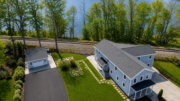A two-story house with a large front lawn, a separate garage, and a view of a lake and railway tracks. - Seneca Wine Trail | Near Seneca & Cayuga Lake (Seneca Falls)