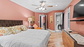 A bedroom with a tufted headboard, a bed with patterned pillows, a ceiling fan, a dresser, and a television on the wall. - Seneca Wine Trail | Near Seneca & Cayuga Lake (Seneca Falls)
