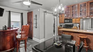 A modern kitchen with a glass dining table, wooden chairs, a bar area, and a ceiling fan. - Seneca Wine Trail | Near Seneca & Cayuga Lake (Seneca Falls)