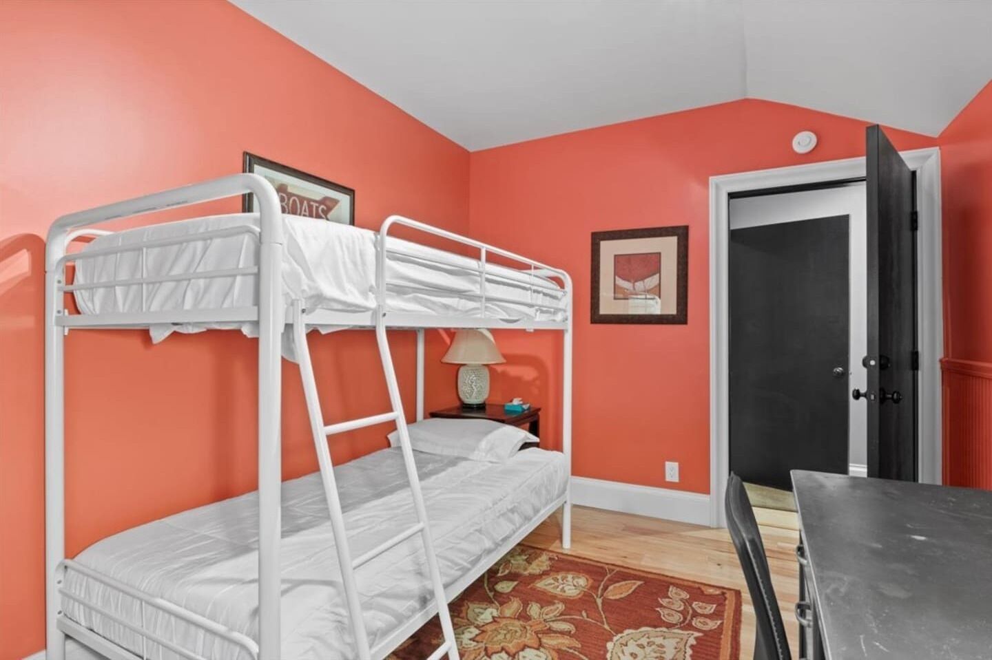 A bunk bed room with orange walls, a door, and a small table.