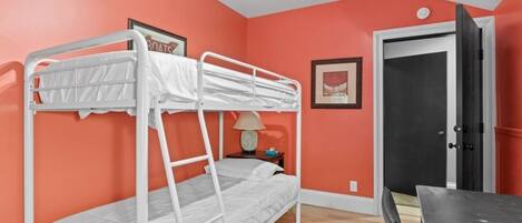 A bunk bed room with orange walls, a door, and a small table.