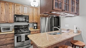A kitchen with wooden cabinets, a stainless steel refrigerator, a microwave, a stove, a coffee maker, and a granite countertop. - Seneca Wine Trail | Near Seneca & Cayuga Lake (Seneca Falls)