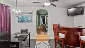 A modern living room with a dining area, a TV mounted on the wall, and a staircase leading to another room. - Seneca Wine Trail | Near Seneca & Cayuga Lake (Seneca Falls)