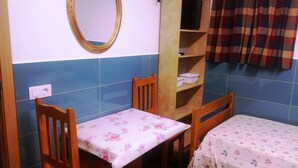 A small room with two wooden chairs, a table with a floral tablecloth, a mirror with a gold frame, a shelf with white bowls, and a plaid curtain. - COLIVING 87 STUDIO NUMBER 1 (L'Hospitalet de Llobregat)