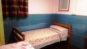 A small, single-bed room with a wooden headboard, a floral-patterned bedspread, and a checkered curtain. - COLIVING 87 STUDIO NUMBER 1 (L'Hospitalet de Llobregat)