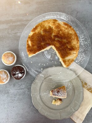 A round cake on a clear glass plate with a slice cut out, dusted with powdered sugar.