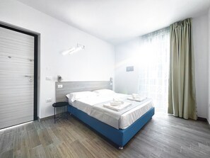 A modern hotel room with a large bed, a bedside table, and a view of the city through the window.