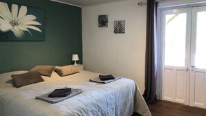 Un dormitorio con una cama grande, dos almohadas, una mesita de noche con una lámpara y una ventana con cortinas.