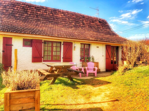 A rustic house with a tiled roof, a wooden table, and two pink chairs in the yard. - Lascaux Countryside Gite - Family run and pet friendly (MONTIGNAC)