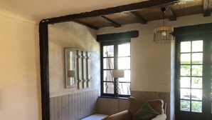 Una habitación con un banco de madera, un sillón acolchado, un espejo y una ventana con vistas a follaje.