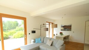 Een moderne woonkamer met een grijze modulaire bank, een witte salontafel en een eethoek met een tafel en stoelen.