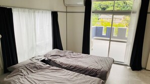 A bedroom with two beds, a window with curtains, and an air conditioning unit. - AZ Hotel Minamiawaji (Minamiawaji)