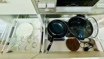 A kitchen drawer with various kitchenware including plates, bowls, a frying pan, a wok, and a spatula.