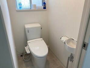 A small, clean bathroom with a toilet, a sink, and a window above the toilet.