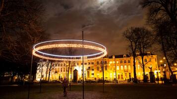 Une vue nocturne d’un parc, avec une installation lumineuse circulaire et un bâtiment en arrière-plan.