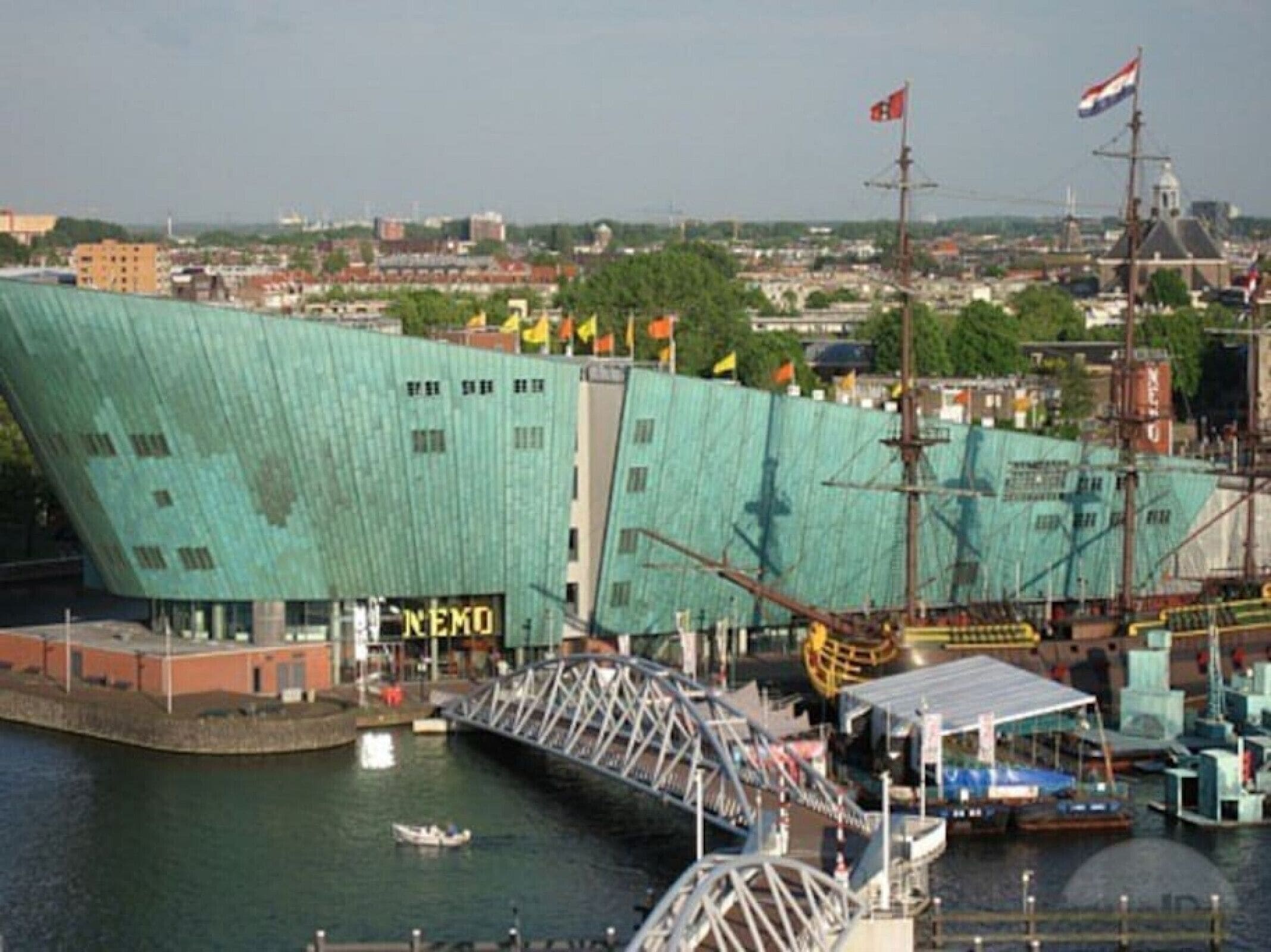 Un grand bâtiment moderne doté d’une façade verte originale, d’une enseigne bien visible portant l’inscription « NEMO », et d’une structure en forme de pont qui s’étend au-dessus d’une étendue d’eau.
