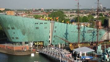Un grand bâtiment moderne doté d’une façade verte originale, d’une enseigne bien visible portant l’inscription « NEMO », et d’une structure en forme de pont qui s’étend au-dessus d’une étendue d’eau.