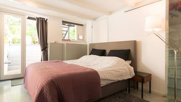 Une chambre à coucher comprenant un lit, une table de chevet, une lampe et une porte-fenêtre coulissante donnant sur un espace extérieur.