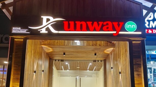 En hotellentrén med en träfasad, en trappa som leder inåt, och skyltar för ”Runway Inn” och ”Rum och restaurang”.
