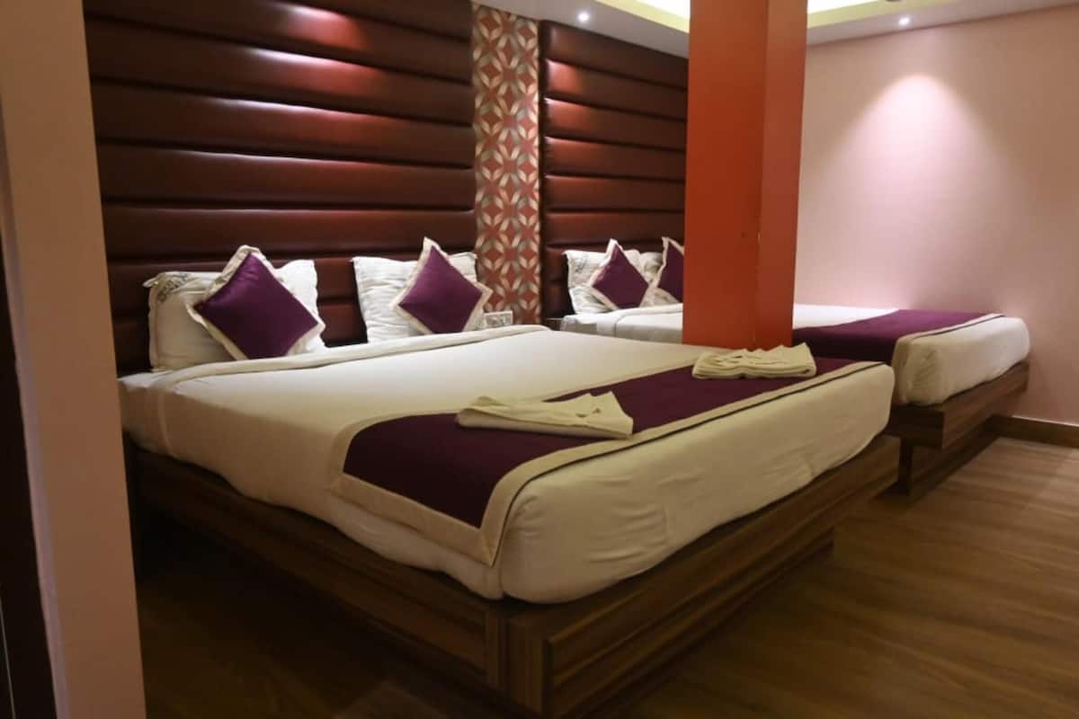 A hotel room with two beds, each with white linens and purple pillows, a wooden headboard, and a patterned column.